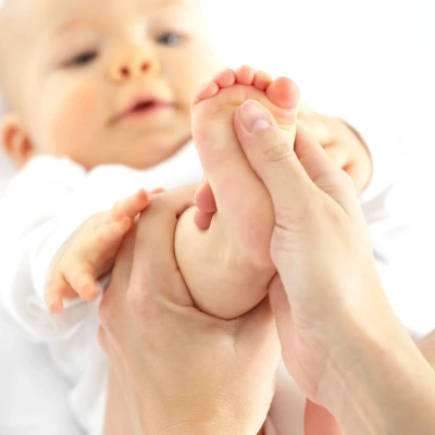 mains d’un adulte massant doucement le pied d’un bébé allongé