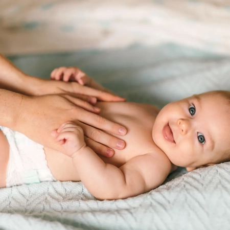 Bébé souriant allongé sur une surface douce recevant un massage relaxant des mains d’une professionnelle de la petite enfance